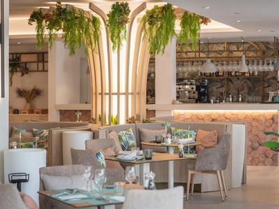 Intérieur de restaurant moderne avec plantes sur pilier lumineux central et tables élégantes.