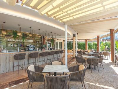 Bar lumineuse avec chaises et tables sous un grand auvent dans un espace extérieur d'hôtel.