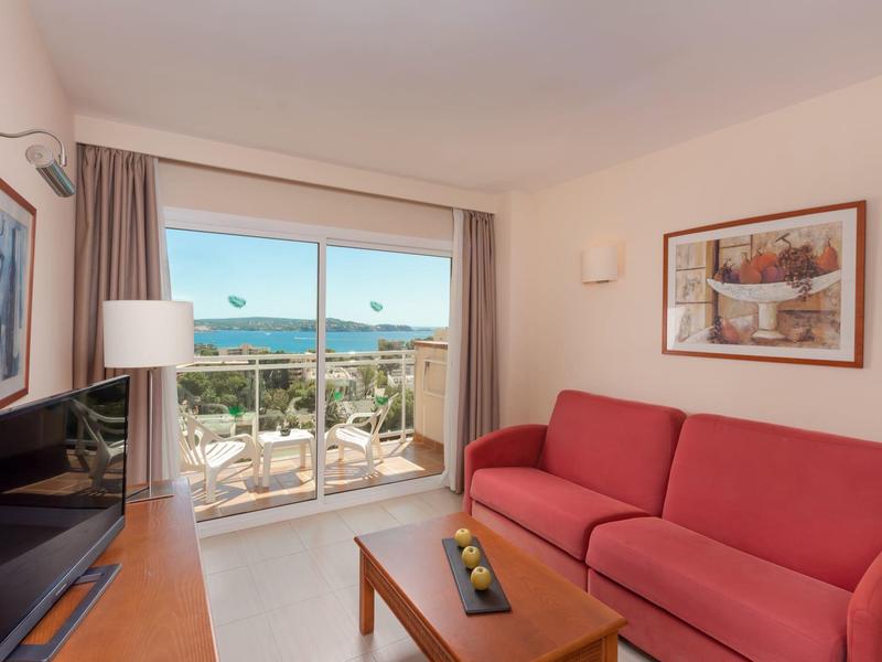 Salon lumineux avec canapé rouge, grande fenêtre et vue sur terrasse et mer.