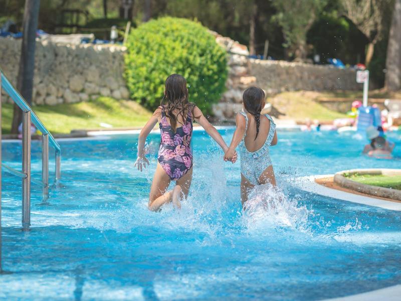 Deux enfants courent main dans la main dans une piscine extérieure par une journée ensoleillée.