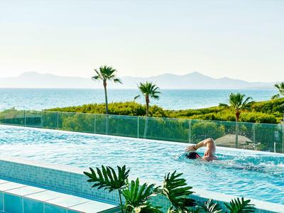 Nuotatore in piscina a sfioro con vista su palme e montagne.