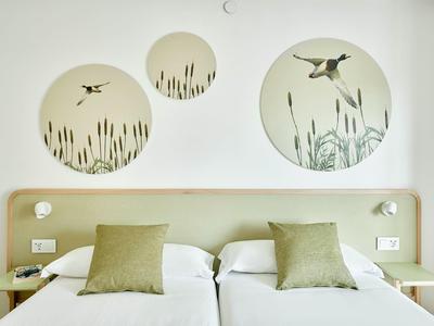 Simple hotel room with two single beds and bird-themed wall decorations.