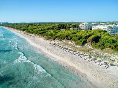 Spiaggia di sabbia bianca con ombrelloni e mare turchese davanti a dune verdi e hotel.