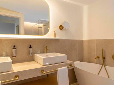 Bagno moderno in hotel con lavandino, grande vasca da bagno e rubinetteria dorata.