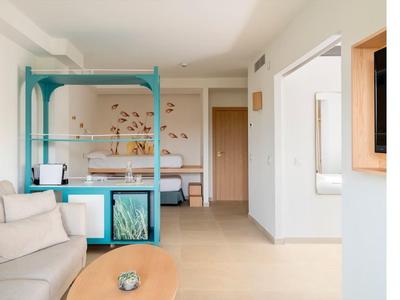 Camera d'hotel moderna con divano, tavolino in legno e letto matrimoniale sullo sfondo.