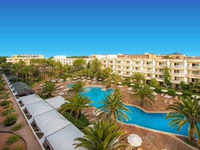 Große Hotelanlage mit geschwungenem Pool, Palmen und blauen Himmel im Hintergrund.