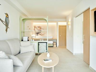 Moderner Hotelzimmer mit grauem Sofa, rundem Tisch und Vogel-Wandkunst.