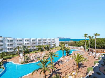 Moderner Hotelkomplex mit großem Pool, Palmen und klar blauem Himmel im Urlaubsort.