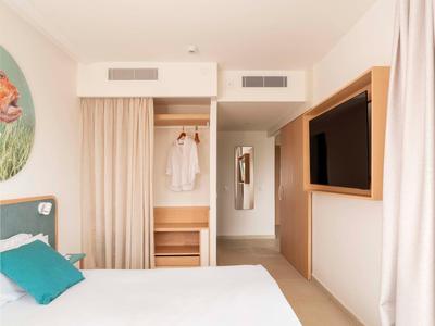 Schlafzimmer mit offenem Kleiderschrank, Bett mit Kissen und Wandfernseher.