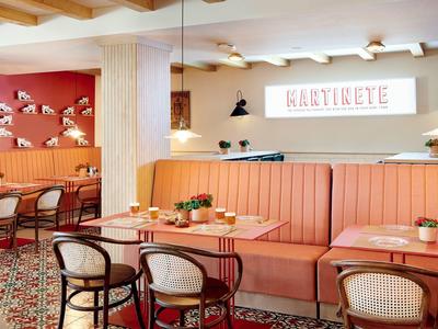 Gezellige kantine met pasteloranje banken, houten tafels en stoelen in een warme sfeer.