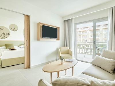 Lichte hotelkamer met moderne bank, fauteuil, salontafel en balkon met stadszicht.