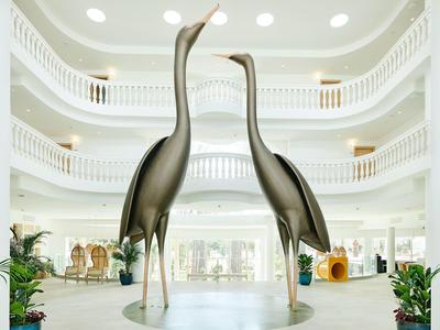 Deux grandes statues dorées de grues dans le hall intérieur d'un hôtel blanc moderne.
