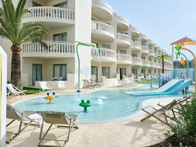 Piscine d'hôtel avec toboggans aquatiques et chaises longues devant un bâtiment moderne.