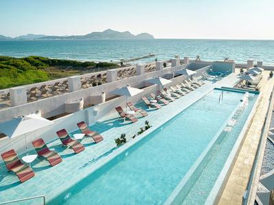 Piscine longue avec chaises longues offrant vue sur la mer et montagnes lointaines.