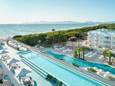 Hôtel avec longue piscine extérieure, transats et vue sur la mer par une journée ensoleillée.
