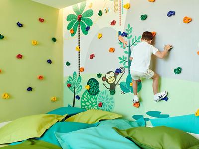 Enfant grimpe un mur d'escalade coloré avec des motifs de jungle dans une pièce lumineuse.