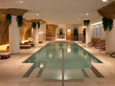 Espace piscine intérieure avec chaises longues et plantes, entouré de rochers et éclairage chaud.