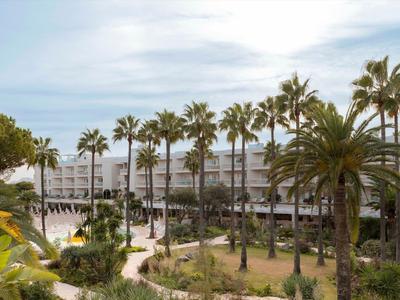 Budynek hotelu wielopiętrowego z palmami na pierwszym planie pod lekko zachmurzonym niebem.