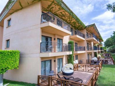 Nowoczesny kompleks hotelowy z balkonami i tarasem w zielonym otoczeniu pod czystym niebem.