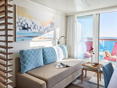 Modern eingerichtetes Hotelzimmer mit Sofa, Kunst an der Wand und Balkon mit Meeresblick.