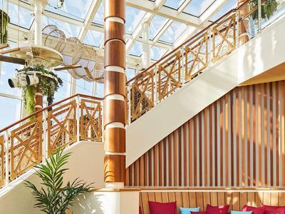 Helles Lounge-Bereich mit Glasdach, Pflanzen und Holzdetails in einem Hotel.