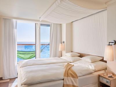 Hell eingerichtetes Hotelzimmer mit zwei weißen Betten und Balkon mit Meerblick.