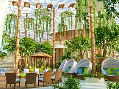 Cour intérieure d'hôtel moderne avec des plantes vertes, des tables à manger et des espaces de détente sous lumière naturelle.