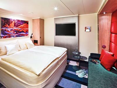 Chambre d'hôtel moderne avec grand lit, coin salon et art mural coloré.