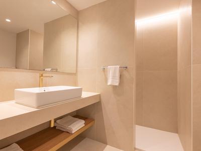 Salle de bain d'hôtel moderne avec lavabo, serviette et douche à l'italienne en tons neutres.