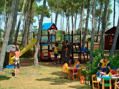 Aire de jeux dans la forêt avec des enfants qui jouent et peignent, entourée d'arbres et de nature.
