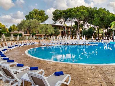 Grande piscine ronde avec chaises longues et serviettes bleues en plein air sous des arbres.