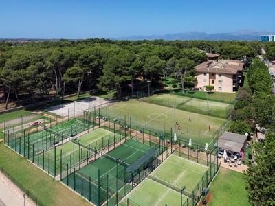 Hotelový areál s tenisovými a paddle tenisovými kurty vedle lesa pod modrou oblohou.