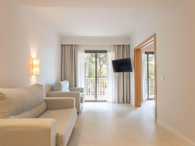 Bright living area with beige sofas and view of a balcony with trees.