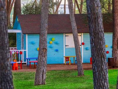 Blue wooden buildings with red doors surrounded by trees on green grass.