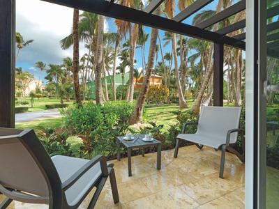 Terrasse mit zwei Stühlen und Tisch, umgeben von Palmen in einem tropischen Garten.