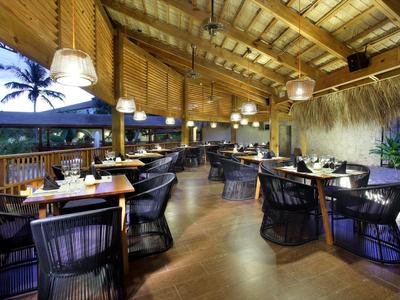 Elegantní restaurace s dřevěnou podlahou a černými proutěnými židlemi pod dřevěným stropem.