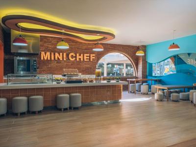 Moderní, světlá mini kuchyňka v hotelu s barovými židličkami a sedacími místy.