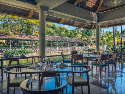 Otevřená restaurace v tropickém resortu s stoly, židlemi a výhledem do zahrady.