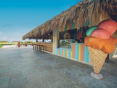Puesto de helados colorido con techo de paja en una playa soleada.
