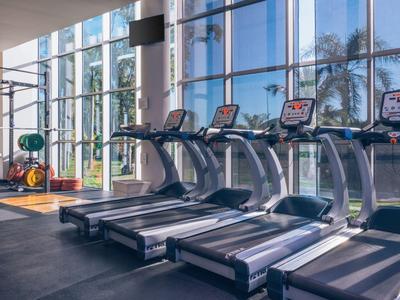 Gimnasio con cintas de correr y pesas frente a grandes ventanas con vista al exterior.
