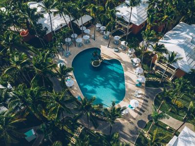Vue aérienne d'une piscine ovale entourée de chaises longues et de palmiers dans un complexe touristique.