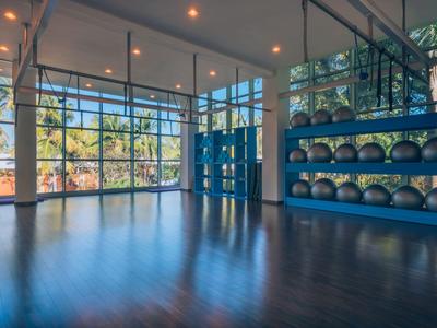 Grote trainingsruimte met houten vloer en spiegels, fitnessballen aan de muur, veel natuurlijk licht.