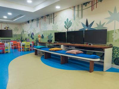 Salle de jeux colorée avec tables, chaises, téléviseurs et décorations murales pour enfants.