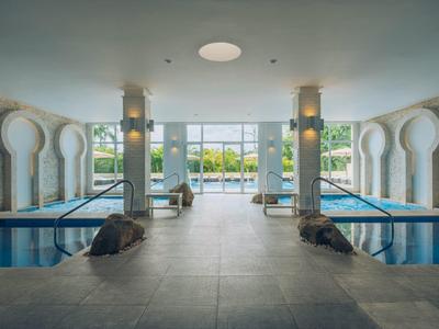 Piscine intérieure luxueuse avec grandes fenêtres donnant sur un paysage extérieur verdoyant.
