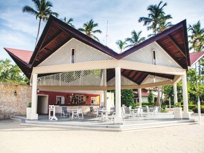 Open beach restaurant with white chairs and tables under a pointed wooden-paneled roof.