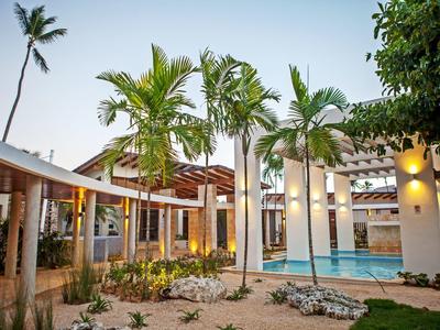 Moderner Hotelbereich mit Pool, beleuchteten Wänden und Palmen bei Sonnenuntergang.