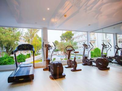 Moderner Fitnessraum mit Geräten, großen Fenstern und Blick auf grünen Außenbereich.