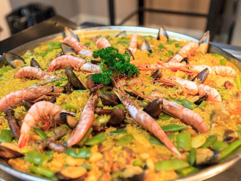 Große Pfanne mit Paella, garniert mit Garnelen und Petersilie.