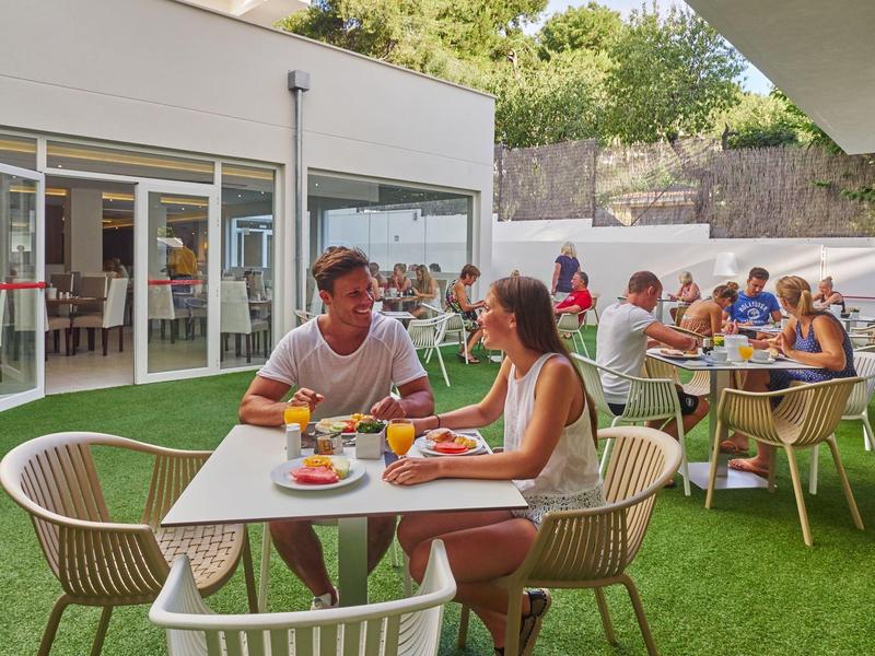 Menschen genießen Mahlzeiten im Freien in einem Restaurant mit grünem Kunstrasen.