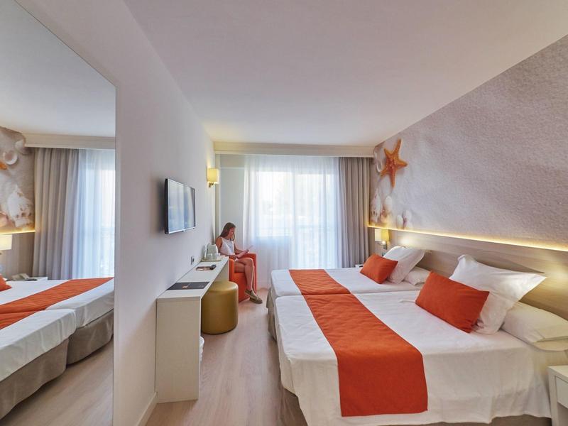 Camera d'hotel moderna con letto matrimoniale, accenti arancioni e finestra con tende.